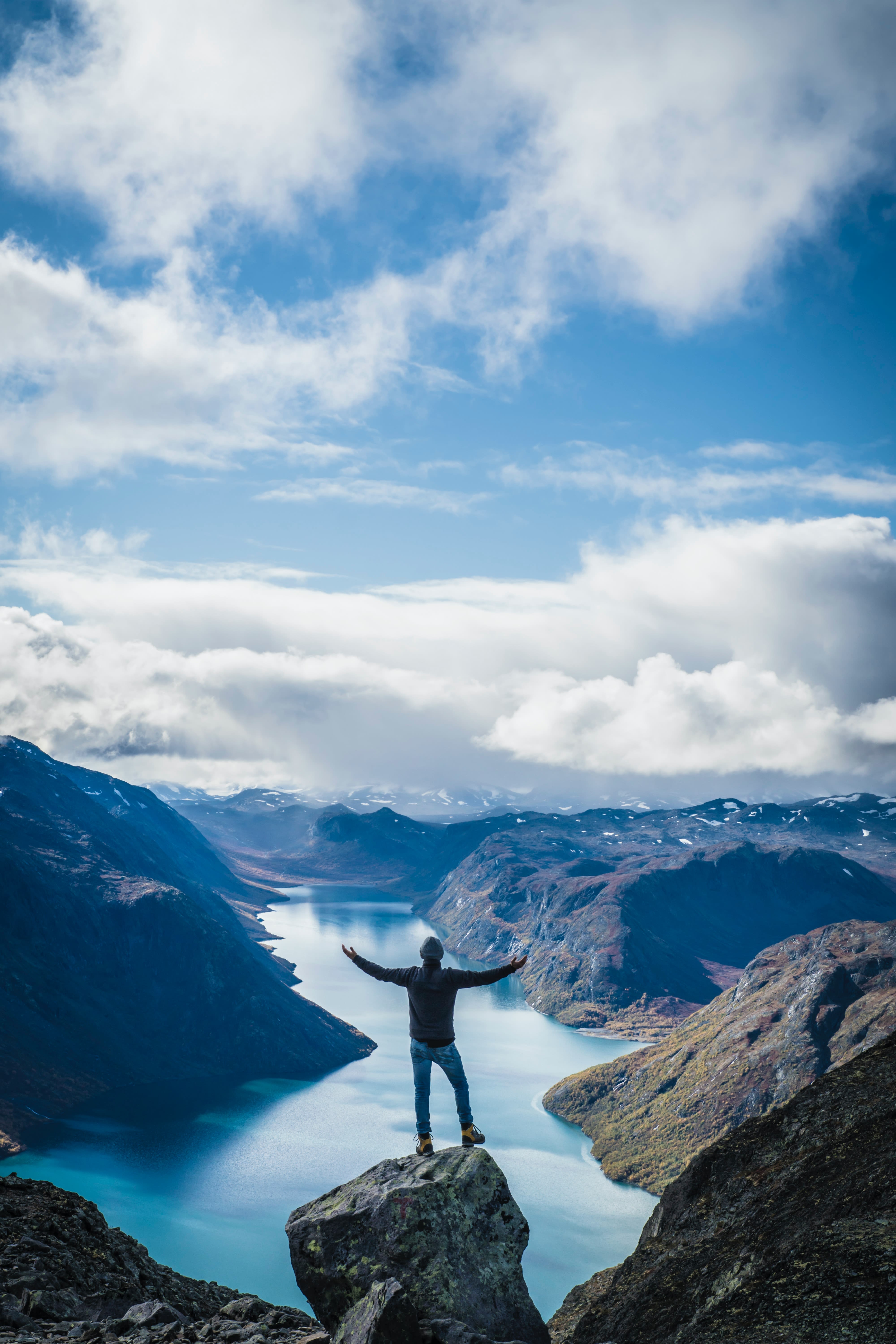 person standing on rock formation near mountains under white clouds during daytime